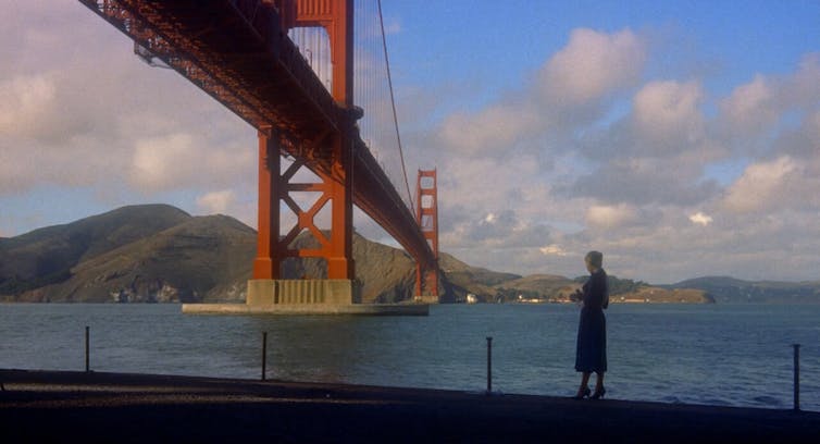 Una mujer pasea al lado de un río con un gran puente rojo, el Golden Gate Bridge, de fondo